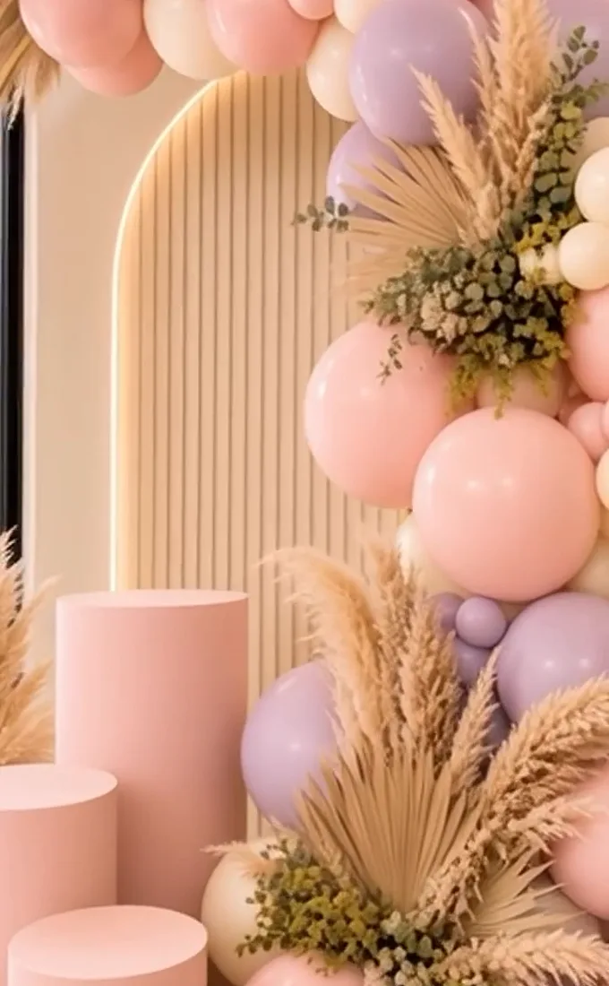 Backdrop de arcos acanalados retroiluminados con globos en rosa palo y lila, pampas y follaje seco.